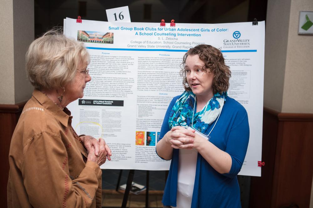 Student presenter speaking to an onlooker as they present their poster
